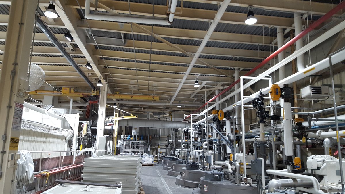 Heavy industrial workshop with dense piping and overhead luminaires in a dusty environment