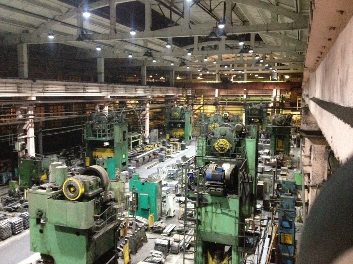 Industrial workshop interior with heavy machinery lit by overhead industrial luminaires