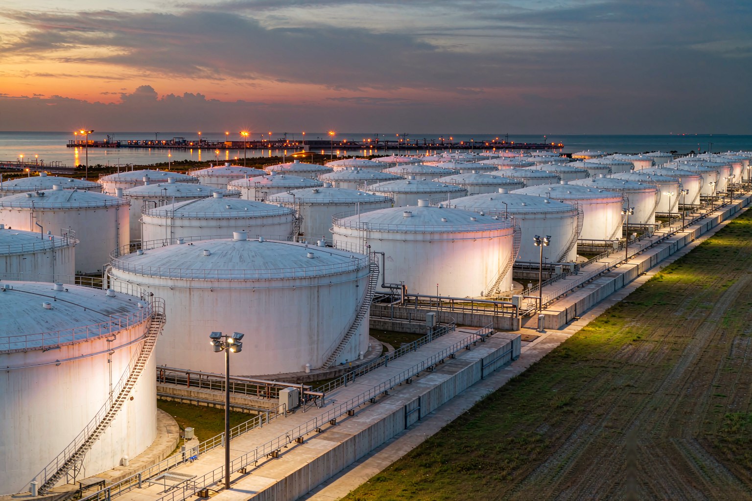 Explosion proof LED linear luminaires along pipe racks and a tank farm at a Jubail petrochemical complex at dusk in Saudi Arabia